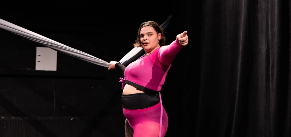 Föreställningsfoto från Body Talks. Linnea Sundblom pekar framåt medan hon håller i ett rep som går tvärs över scenen i axelhöjd.
